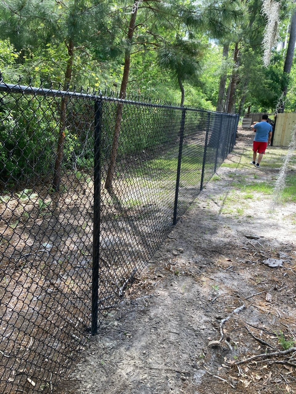 Black chain link fence installation in a wooded Fulshear TX backyard